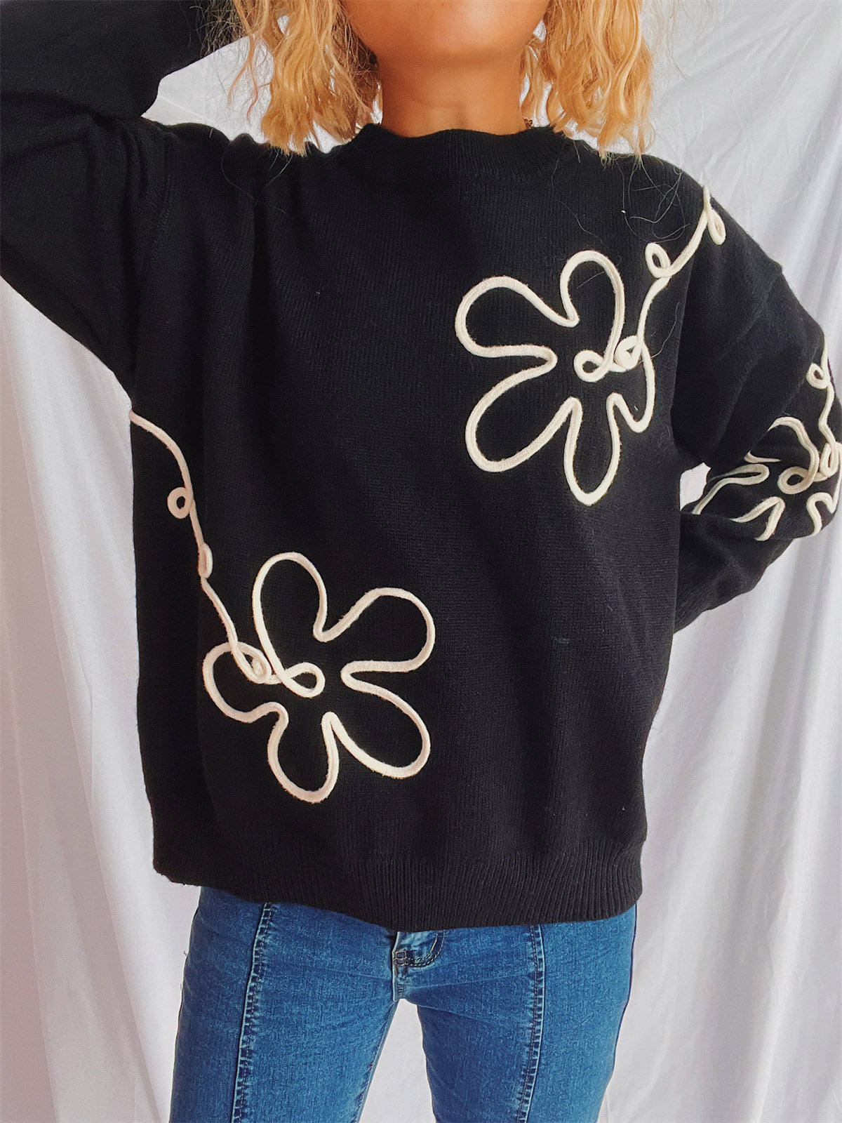 Black knit sweater with cream floral outline pattern, crew neck, long sleeves.