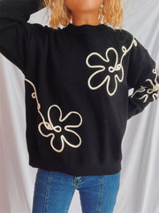 Black knit sweater with cream floral outline pattern, crew neck, long sleeves.