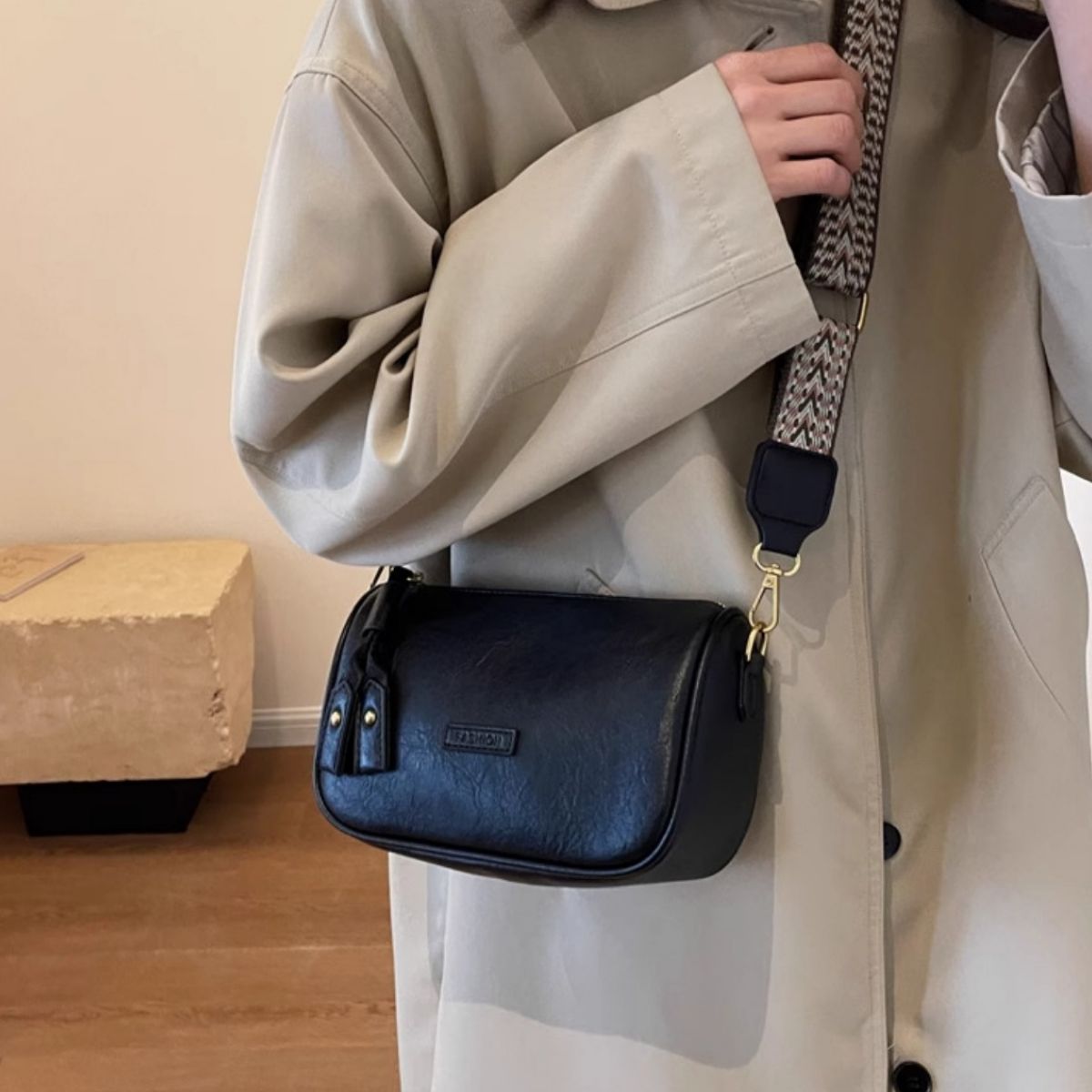 Black textured PU leather crossbody bag with tassel detail and patterned strap.
