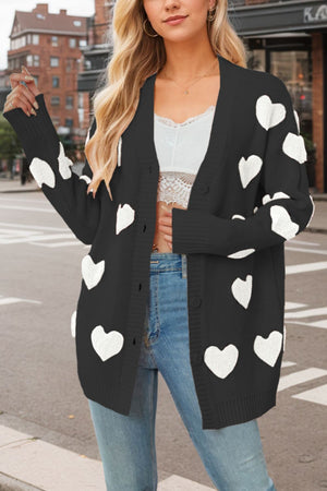 Black knit cardigan with white heart appliqué and buttons, styled with jeans.