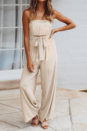 Tan bandeau tie-waist wide-leg jumpsuit with a cropped bodice and flowing pants.