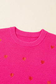 Pink ribbed crewneck sweater with embroidered red hearts, crew neck, long sleeves.