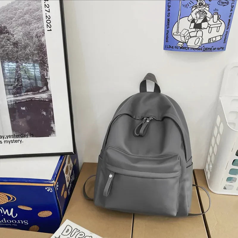 Minimalist dark gray leather backpack with front pocket and zipper details.