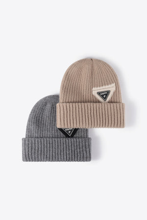 Ribbed acrylic beanies in beige and dark gray, each with a triangular "Happy" patch detail.