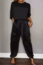 Black satin two-piece ensemble with a belted cargo pant and short-sleeve top.