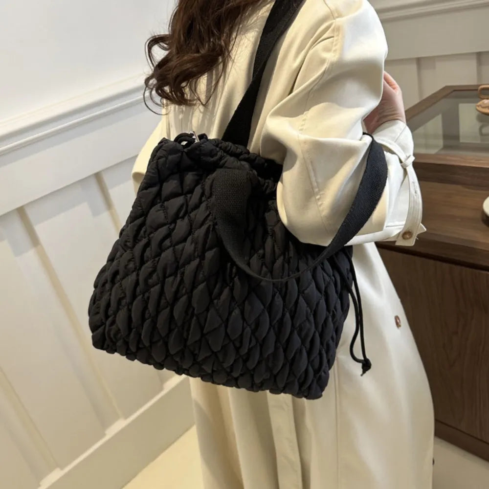 Black quilted drawstring carryall bag with diamond pattern and adjustable straps.