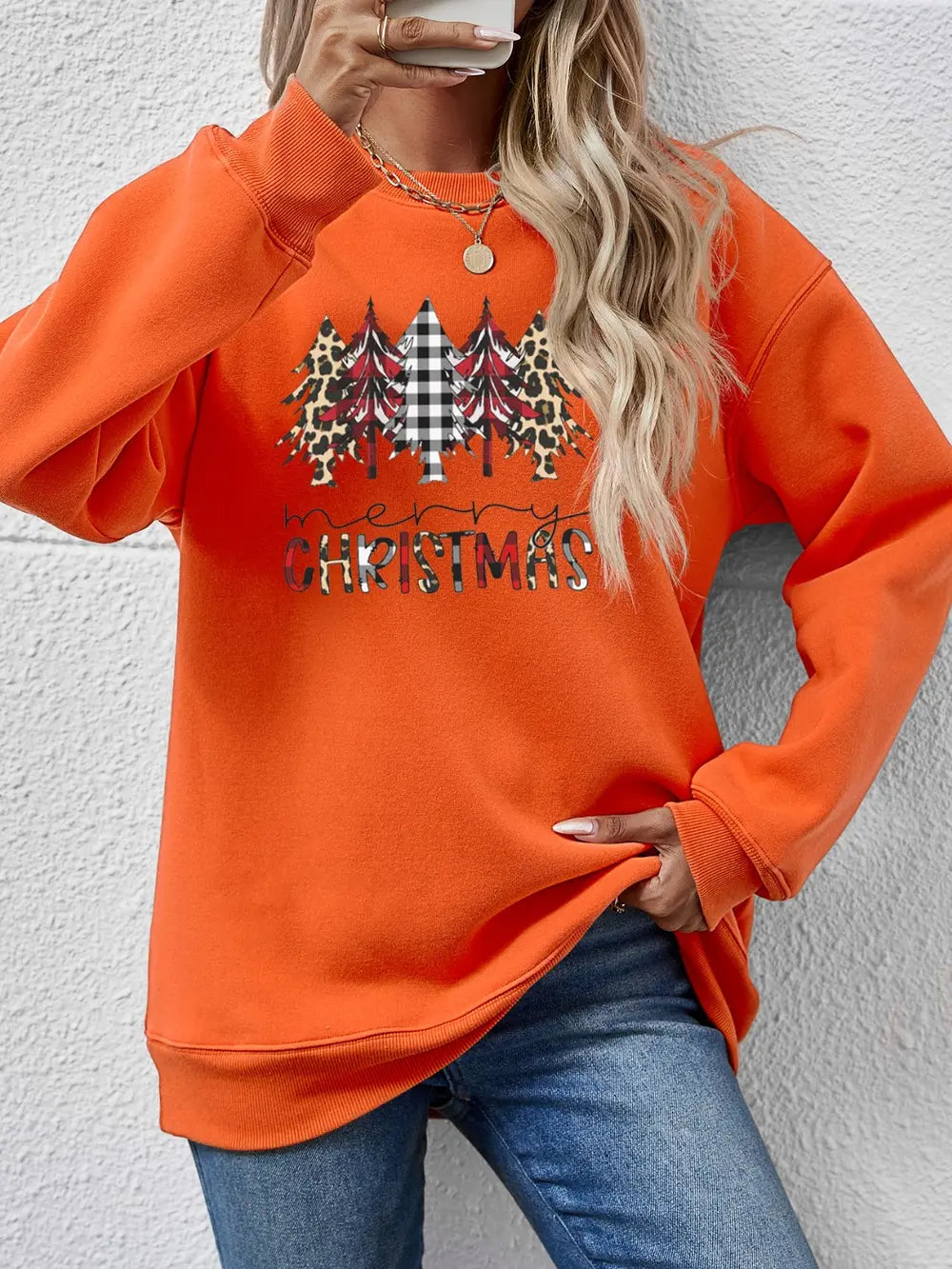 Crewneck sweatshirt in orange with Christmas trees graphic, buffalo plaid, leopard print and Merry Christmas text.