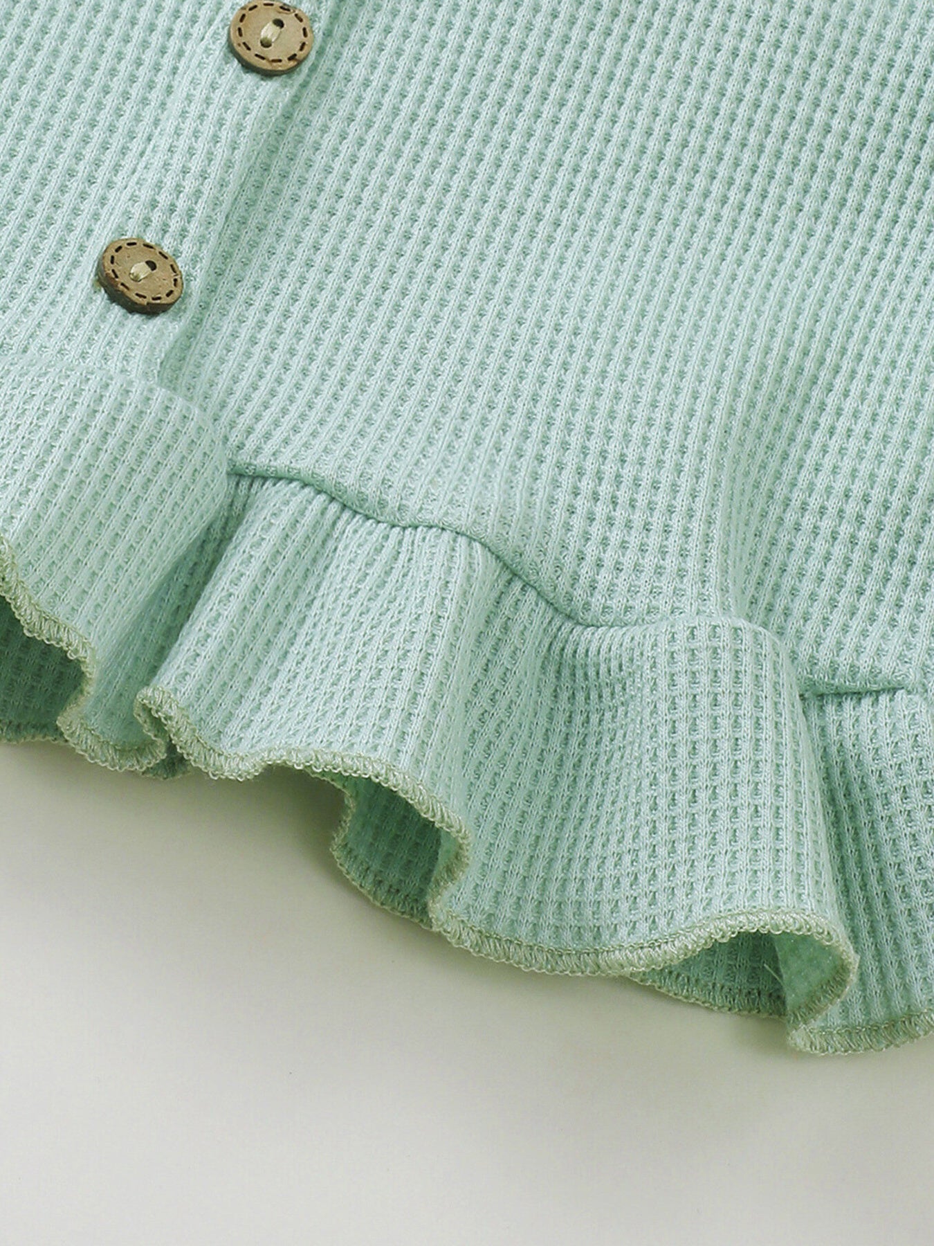 Green waffle knit tank top detail with wooden buttons and ruffled hem.