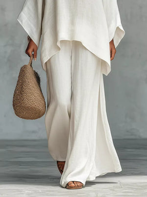 White polyester two-piece set with flowing top and wide-leg pants, styled with a straw bag.