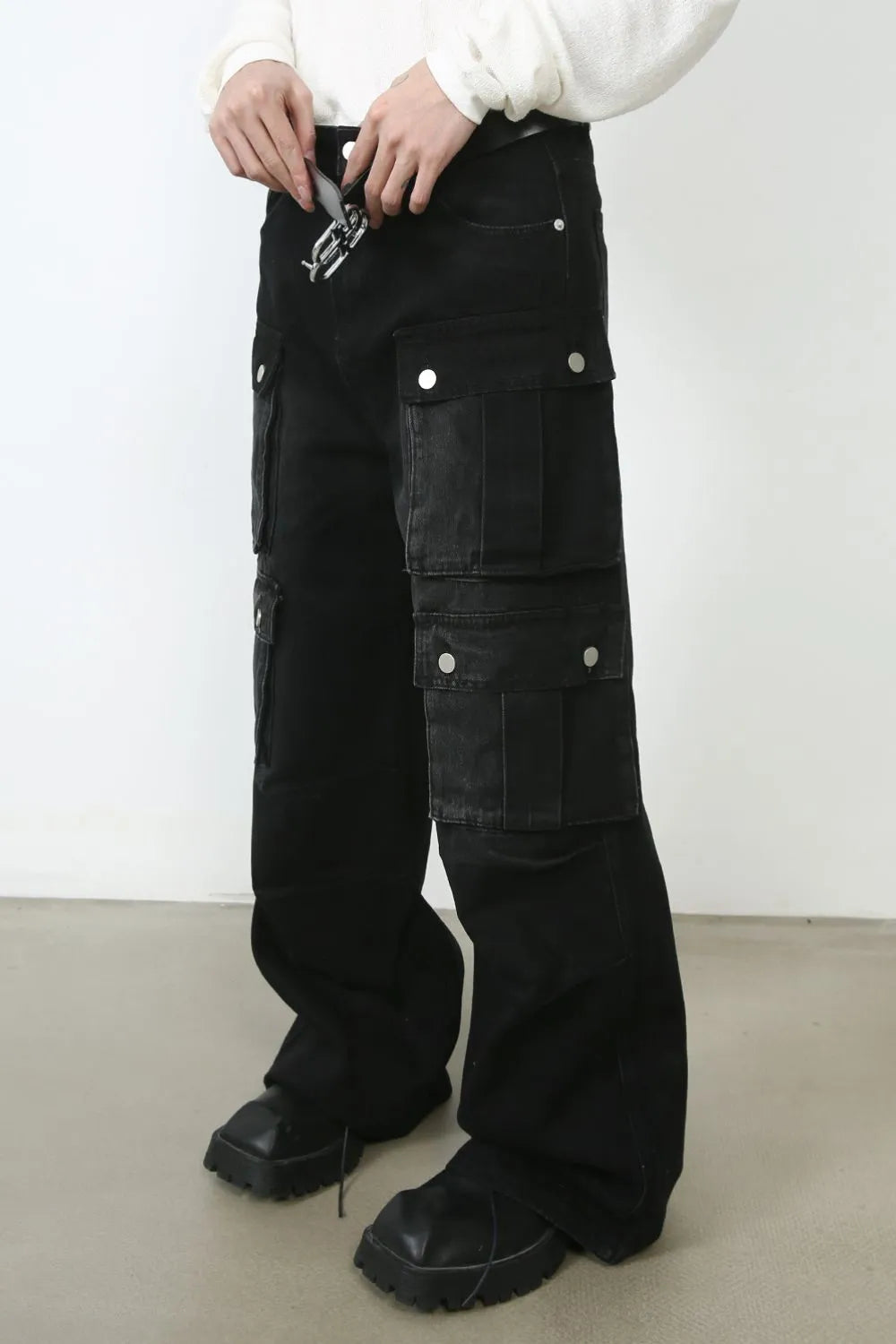 Oversized dark denim cargo pants with multiple pockets and a silver buckle belt detail.