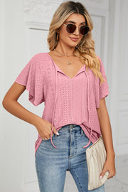 Pink eyelet tie-neck blouse with flutter sleeves and V-neckline.