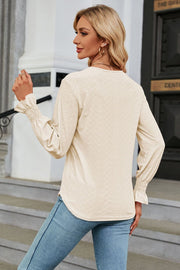 Cream textured V-neck blouse with smocked cuffs and long sleeves.