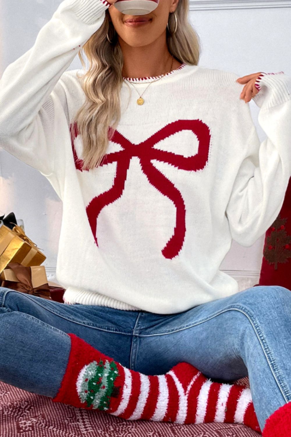 White knit sweater with a large red bow graphic and festive trim.