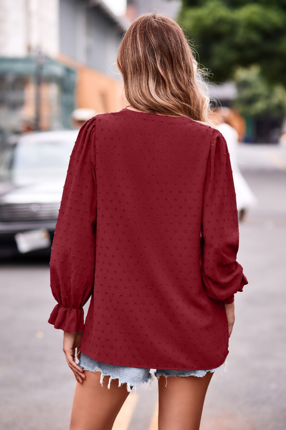 Burgundy textured dot v-neck blouse with ruffle cuffs and long puff sleeves.