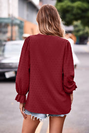 Burgundy textured dot v-neck blouse with ruffle cuffs and long puff sleeves.