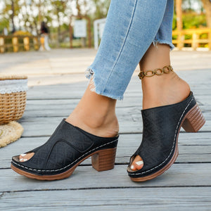 Black peep-toe block heel mules with perforated detail and white stitching.