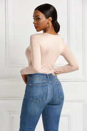 Beige long sleeve bodysuit with a plunging neckline and zip front, styled with denim jeans.