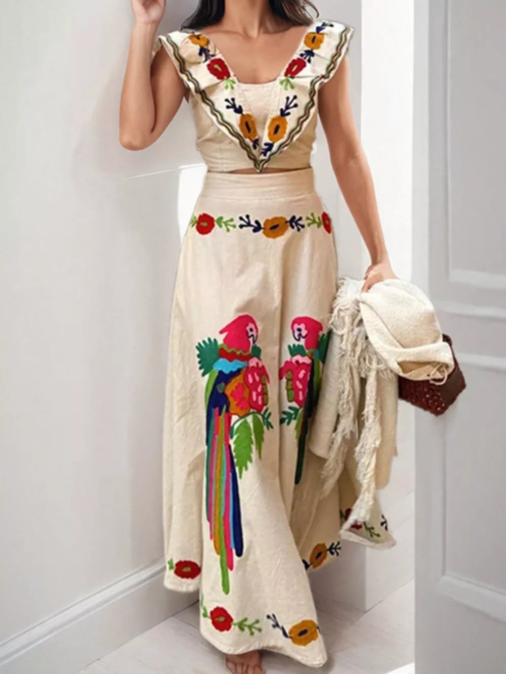 Cream maxi skirt with parrot and floral embroidery, featuring a ruffled V-neck crop top.