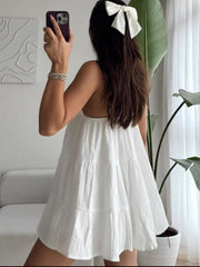 White cotton tiered mini dress with a halter neckline and textured fabric.