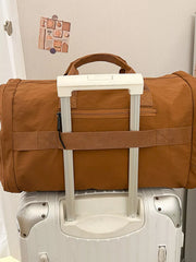 Brown Oxford cloth travel bag with top handles and zippered pockets, resting on a suitcase.