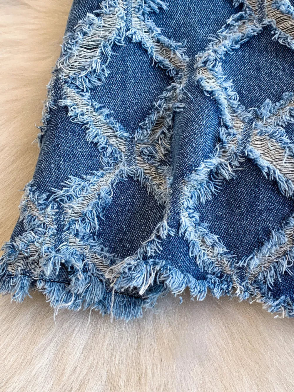 Distressed denim shorts with frayed diamond pattern and raw hem.