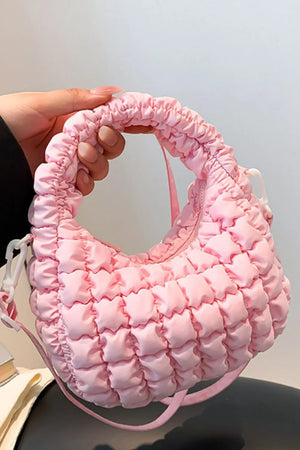 Pink padded crescent crossbody bag with ruched handle and sculptural texture.