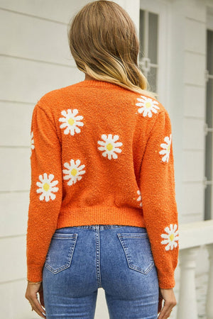 Orange textured knit sweater with white daisy motif, crew neck, long sleeves.