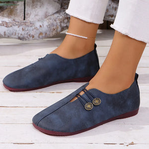 Dark navy leather slip-on flats with antique gold button detail and elastic straps.