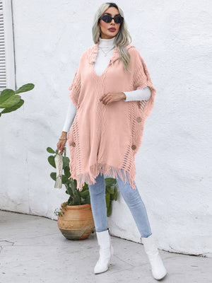 Textured knit poncho in watermelon pink with fringe and wooden buttons, styled with a white turtleneck.