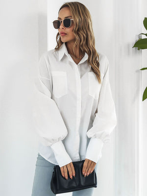 White oversized poplin blouse with blouson sleeves and button front, styled with light wash jeans and a black clutch.