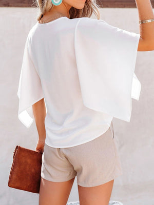 White V-neck blouse with flowy sleeves and a relaxed fit, styled with shorts.
