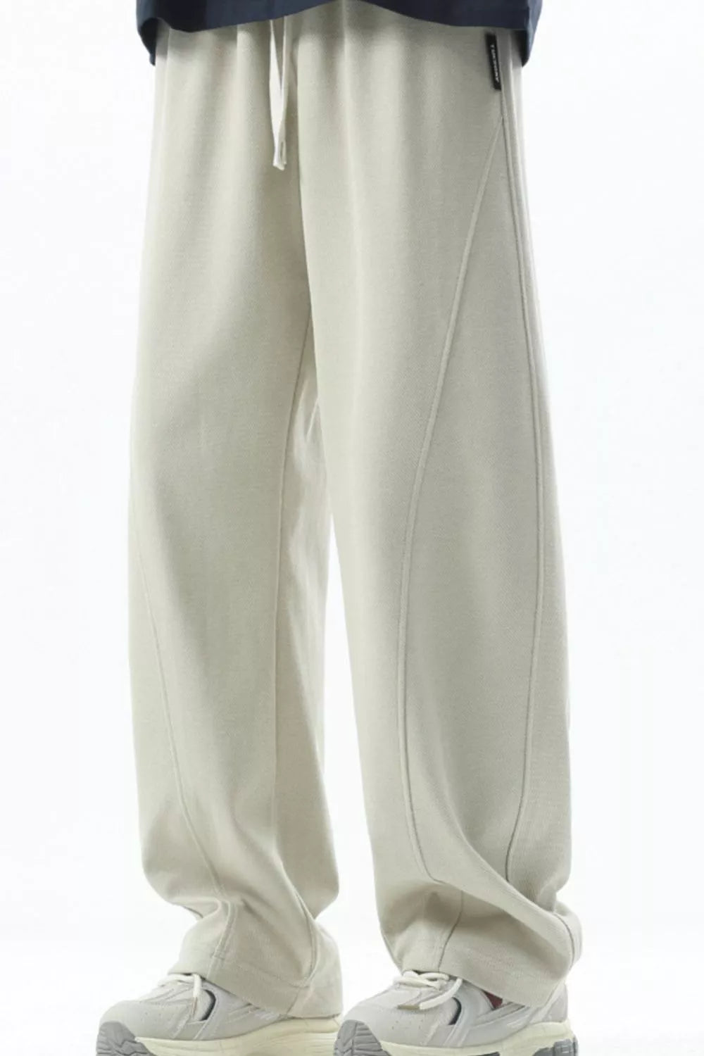 Men's beige loose fit sweatpants with drawstring and curved seam detail.
