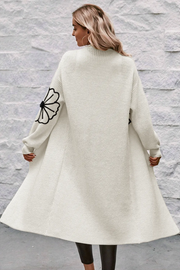 Ivory acrylic maxi cardigan with black floral appliqué on sleeves, open front, long sleeves.
