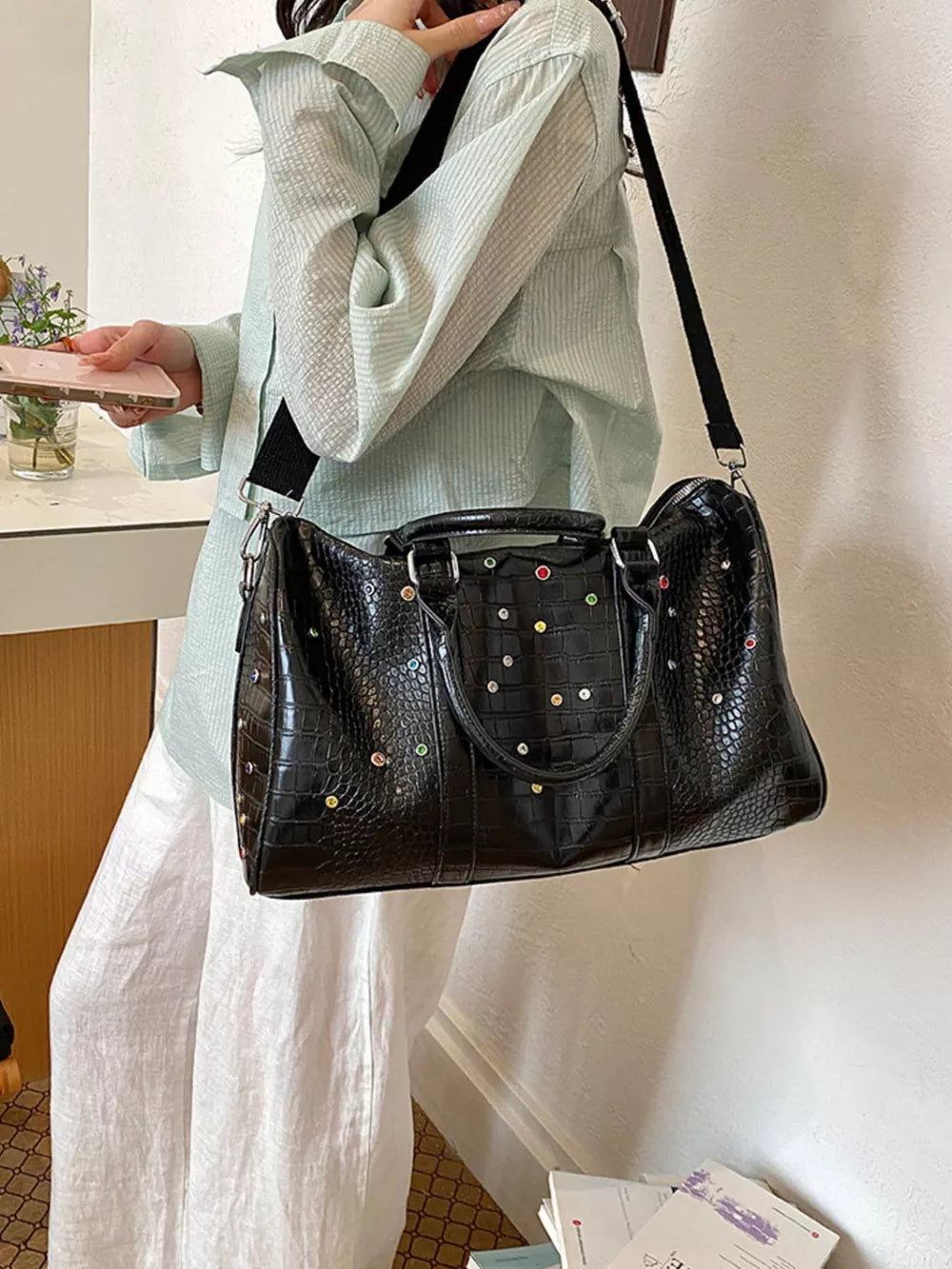 Black crocodile textured duffel bag with colorful stud details and detachable strap.