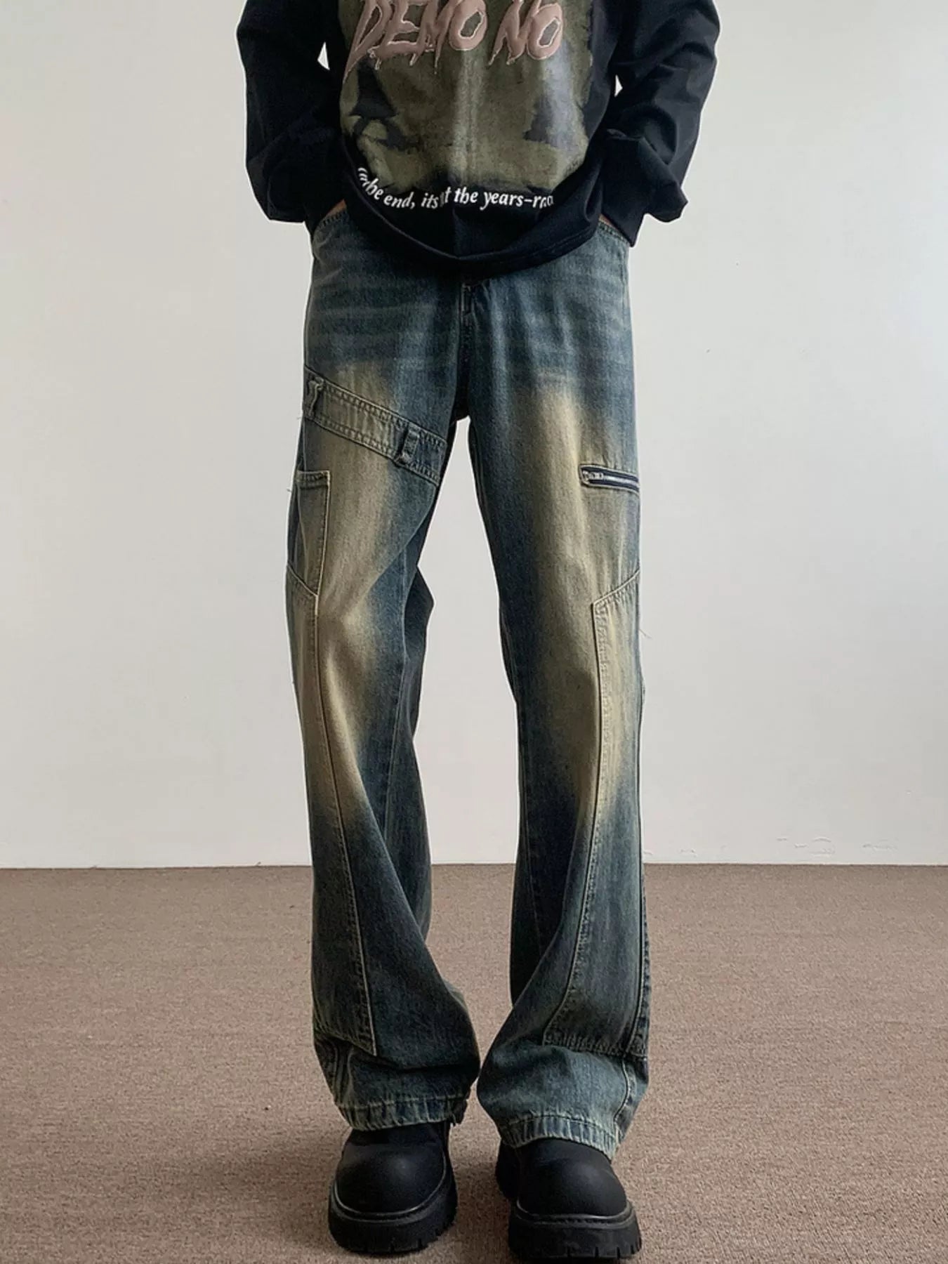 Men's blue vintage wash flare jeans with distressed details and zip pockets.