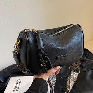 Black textured pu leather crossbody bag with a patterned strap and tassel detail.