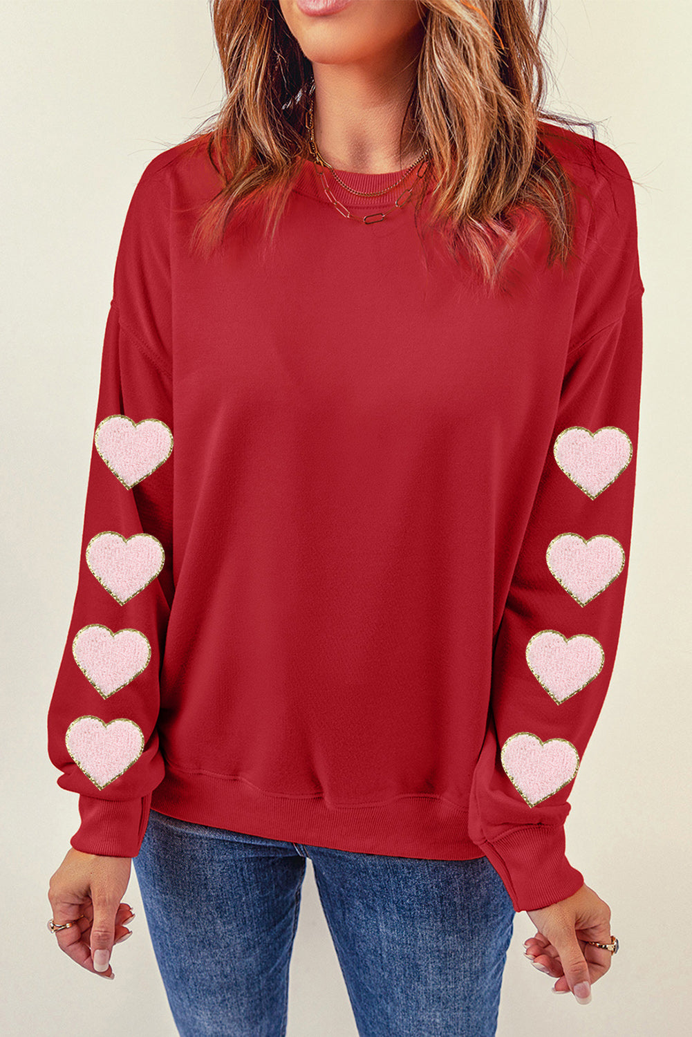 Deep red sweatshirt with pink heart appliqué details on the sleeves.