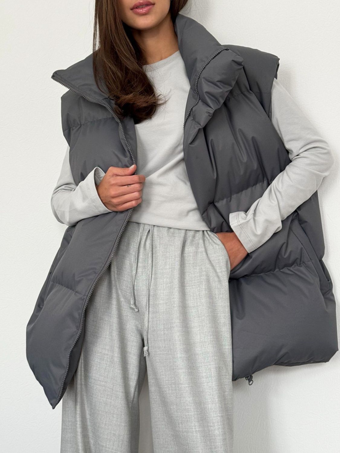 Dark Gray padded puffer vest with a high collar and zip front, styled with a long-sleeve top and trousers.
