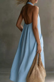 Light blue halter midi dress with pockets and an open back, shown with a straw bag.