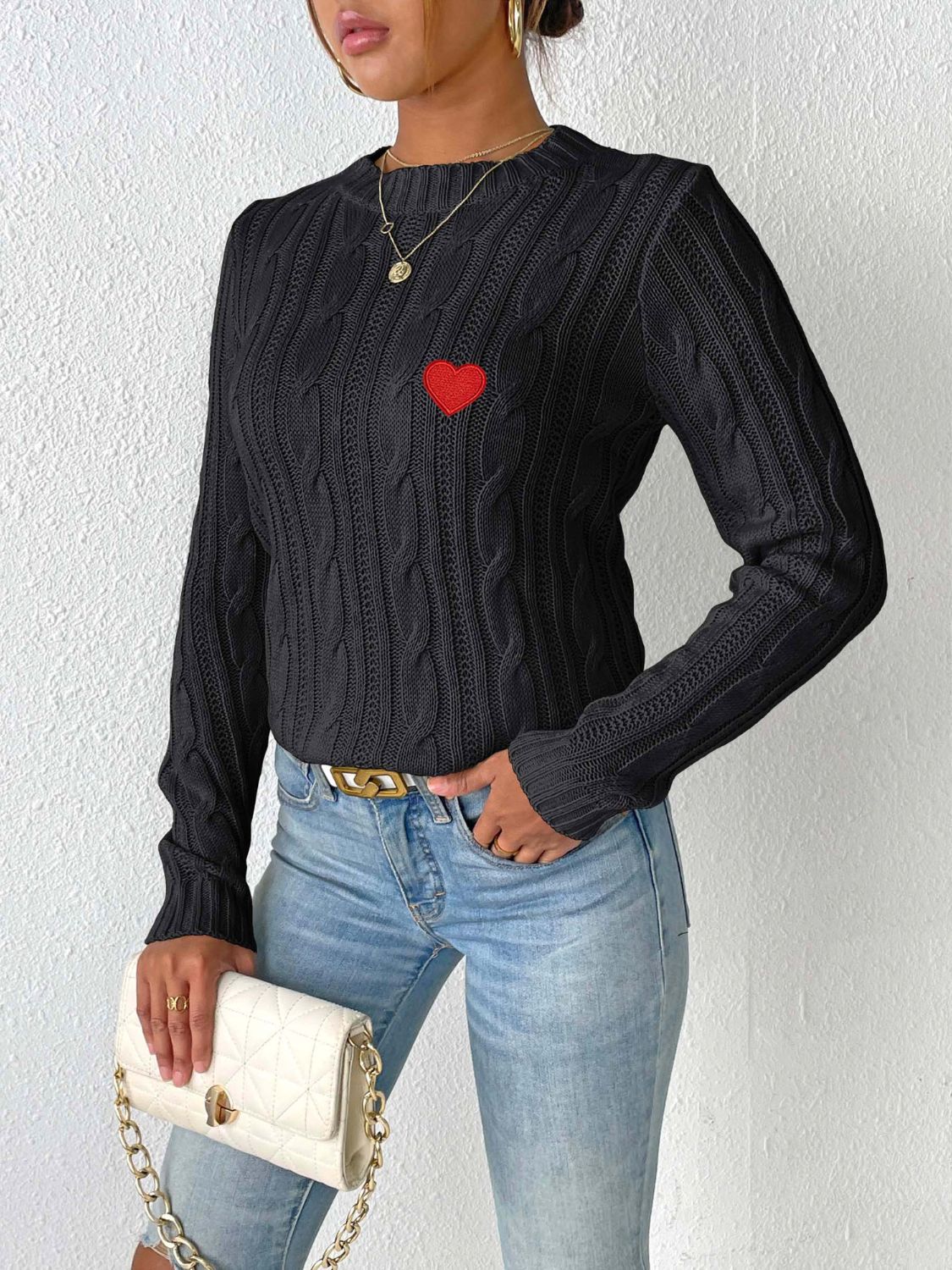 Black cable knit sweater with embroidered red heart detail.