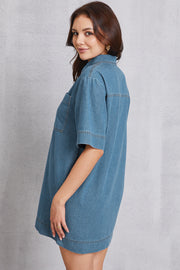 Denim mini dress in medium wash with collared neckline, short sleeves, and chest pockets.