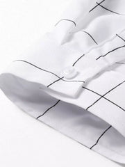 White oversized button-down shirt with black plaid print and button cuff detail.