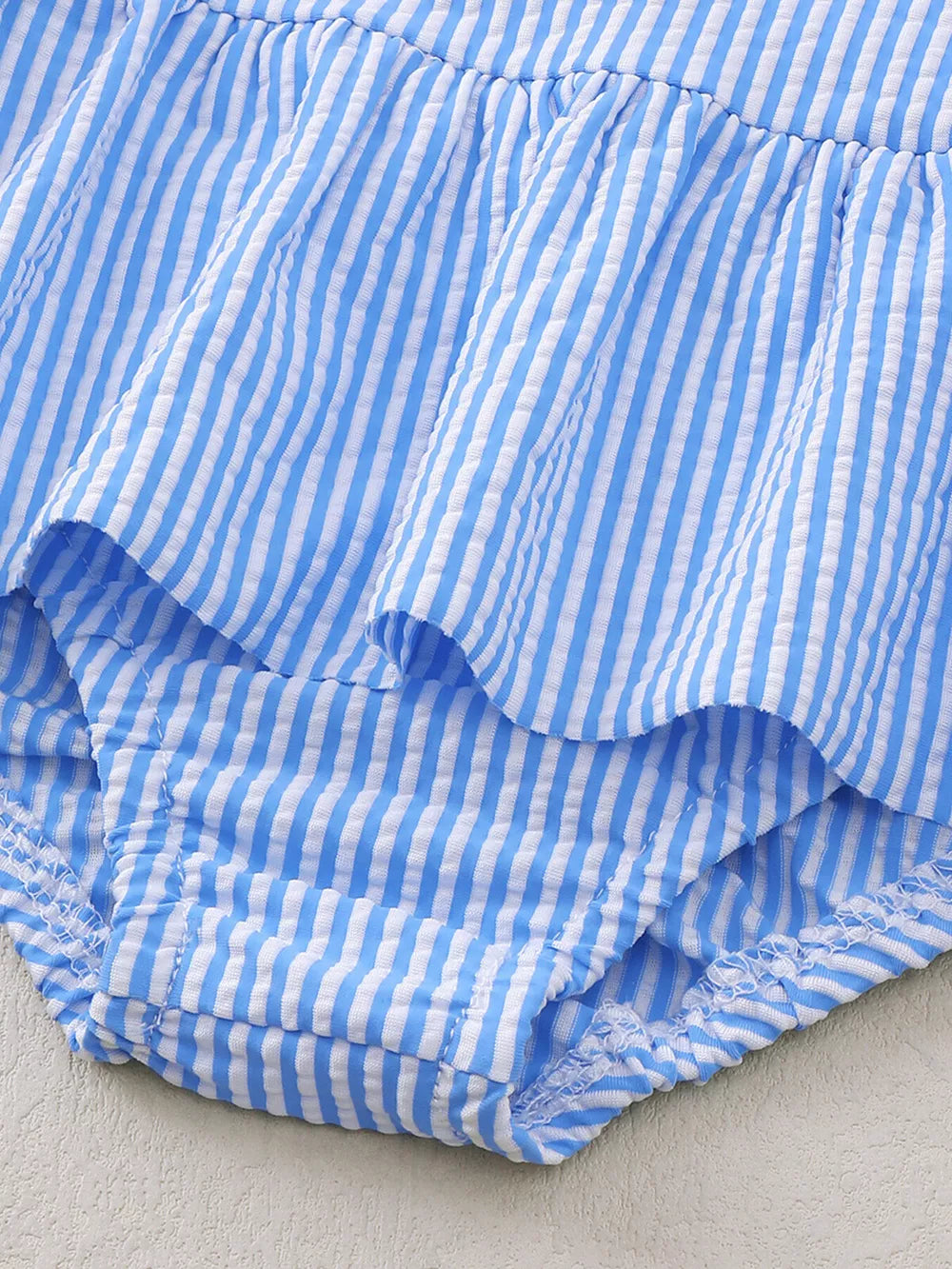 Blue and white striped seersucker one-piece swimsuit with ruffles and a ruffled leg opening.
