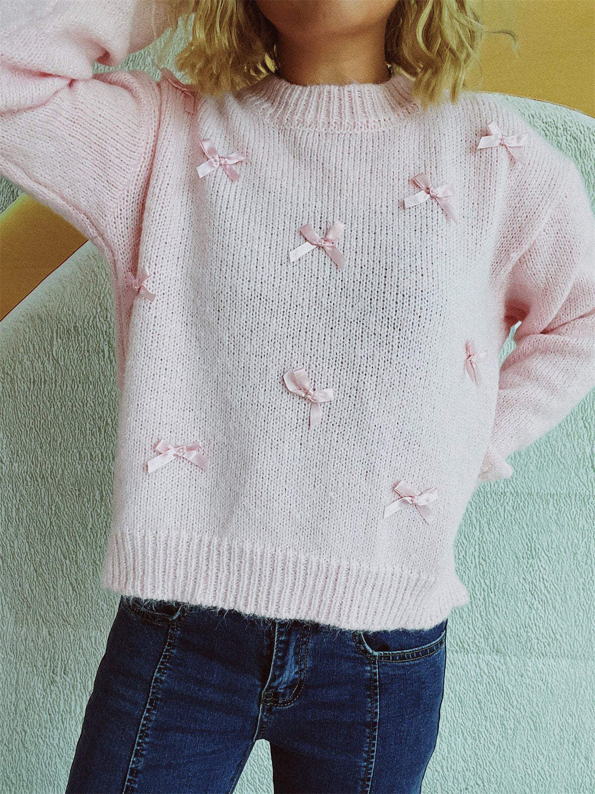 Blush pink knit crewneck sweater with allover pink bow embellishments.