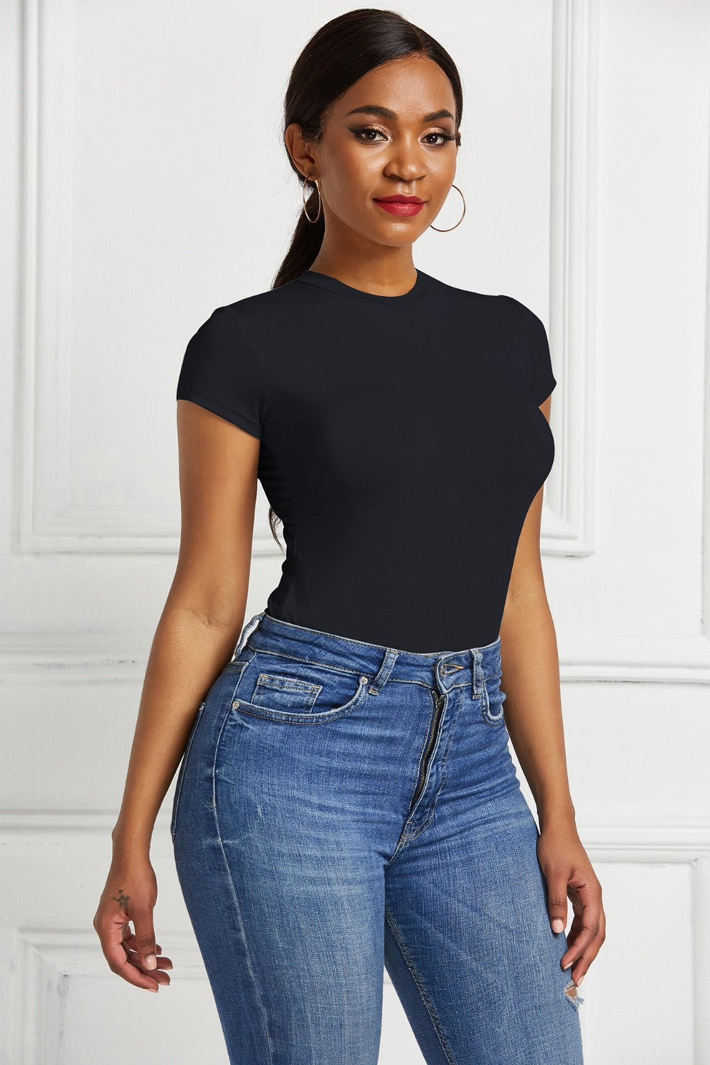 Black crew neck short sleeve bodysuit with a sculpted fit, paired with blue denim jeans.