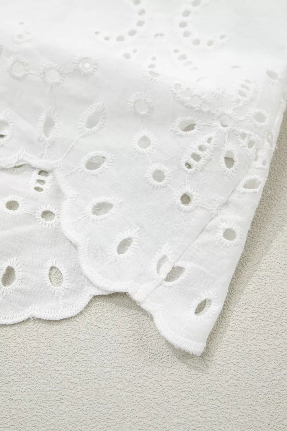 White cotton mini dress with eyelet embroidery and scalloped hem detail.