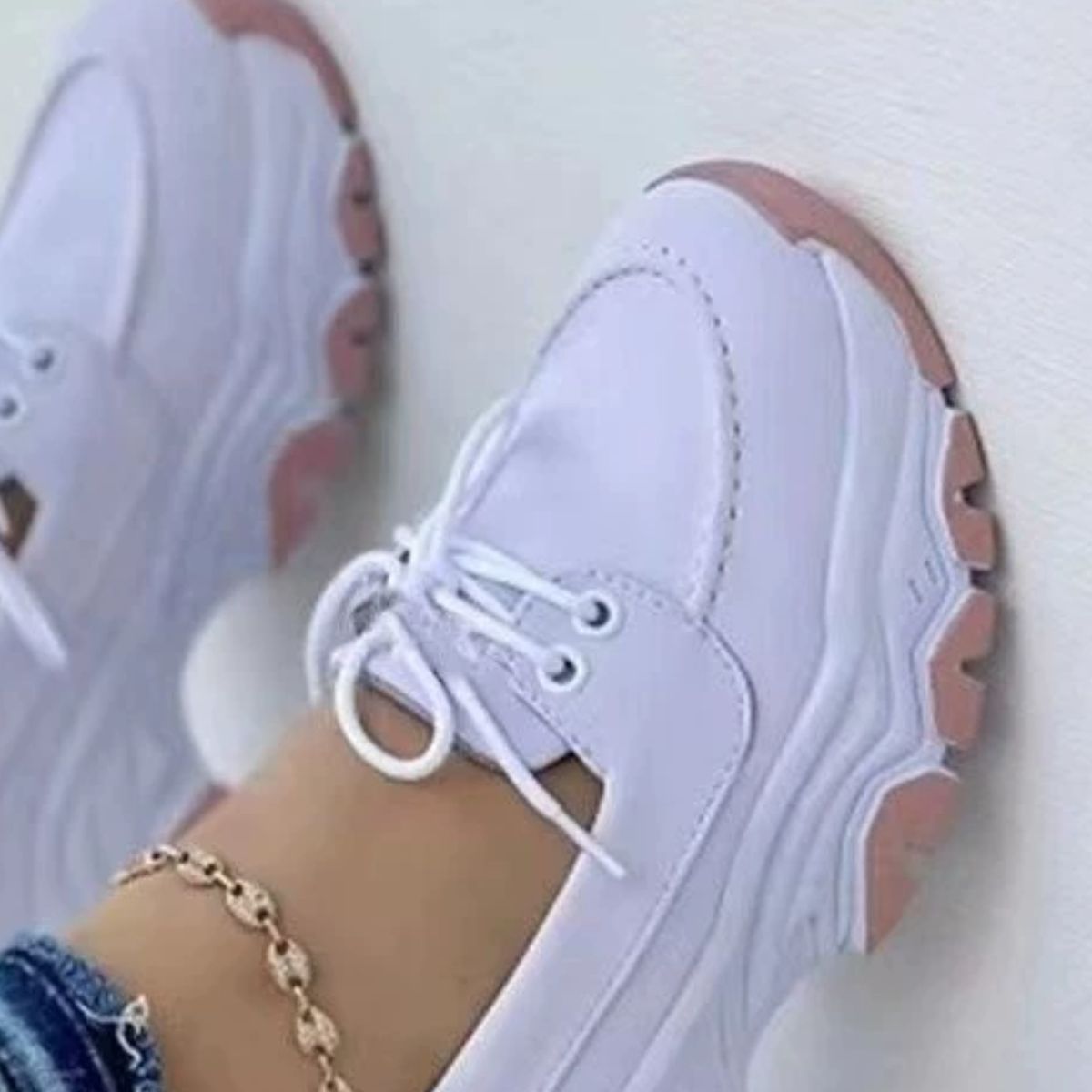 White lace-up sneakers with pink sole detail and round toe.