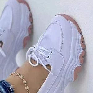 White lace-up sneakers with pink sole detail and round toe.