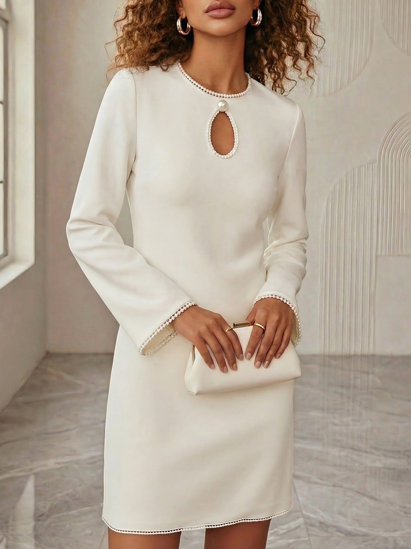White mini dress with pearl trim, keyhole neckline, and long sleeves.