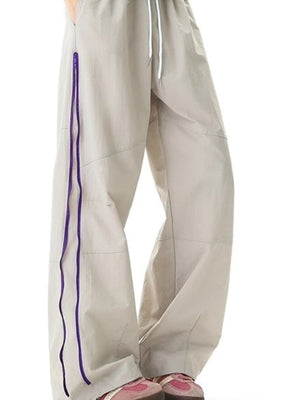 Men's beige loose-fit casual sweatpants with purple zipper detail and drawstring waist.